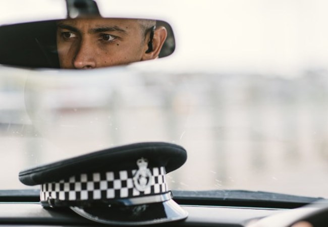 A police officer sat in his car reflected in his interior mirror
