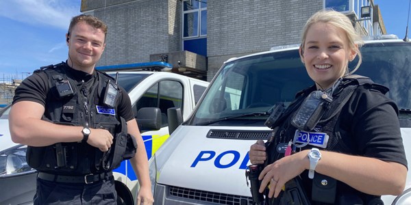 Male and Female officer in uniform smiling in front of Police vehicles.