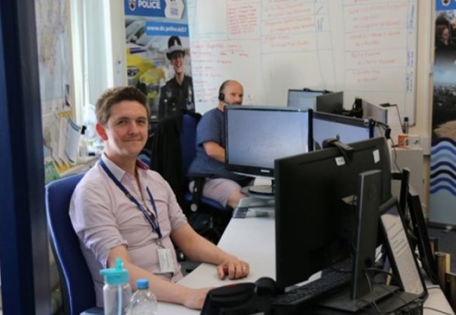 Smiling male police staff member sat at desk