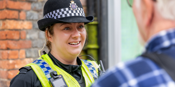Male police officer smiling leaning on countryside fence