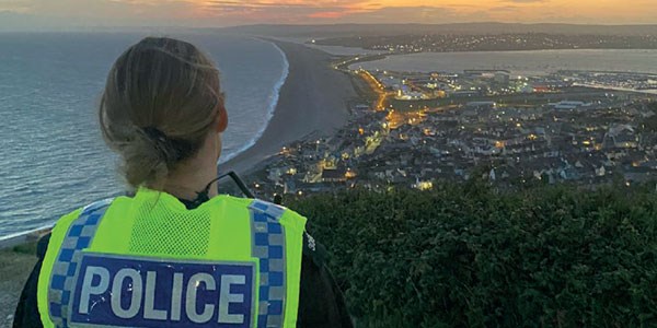 Officer standing looking at a coastal town from a coast path at sunset