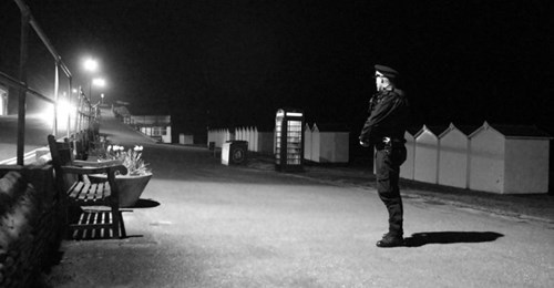 Officer Standing at night on a beach walk way in front of beach huts at night