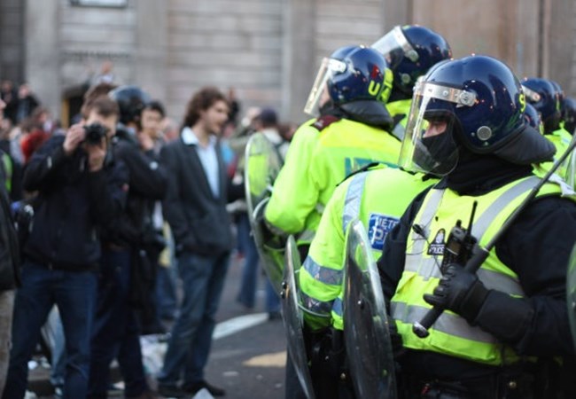 Officers in protective clothing facing a crowd