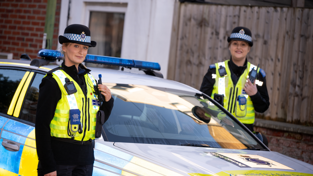 Two female PCSOs standing next to police car
