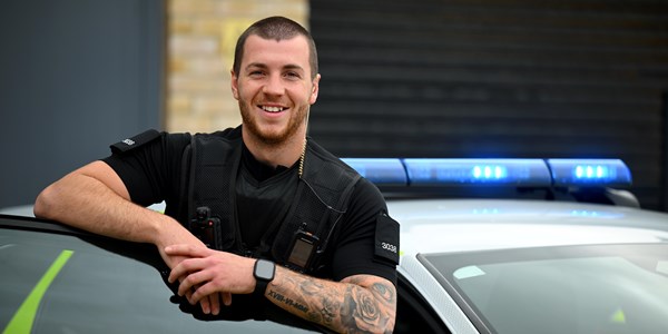 Male Special Constable smiling next to police car