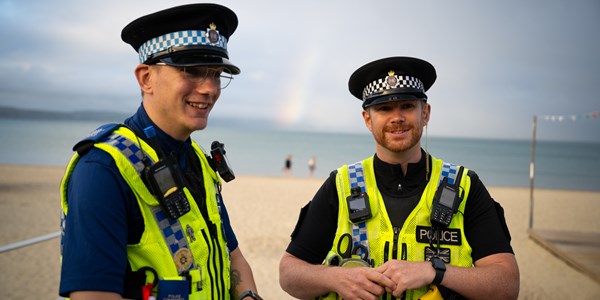A male PCSO and male police officer smiling standing on the beach