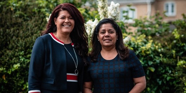 Two female staff members stood infront of hedge